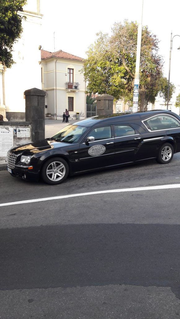 Un carro funebre nero parcheggiato su una strada vicino a un edificio con la facciata bianca.
