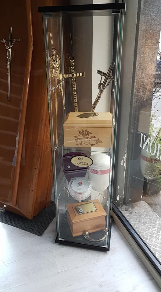 Vetrina con scatole di legno, croci e altri oggetti, probabilmente un monumento commemorativo o un'agenzia di pompe funebri.