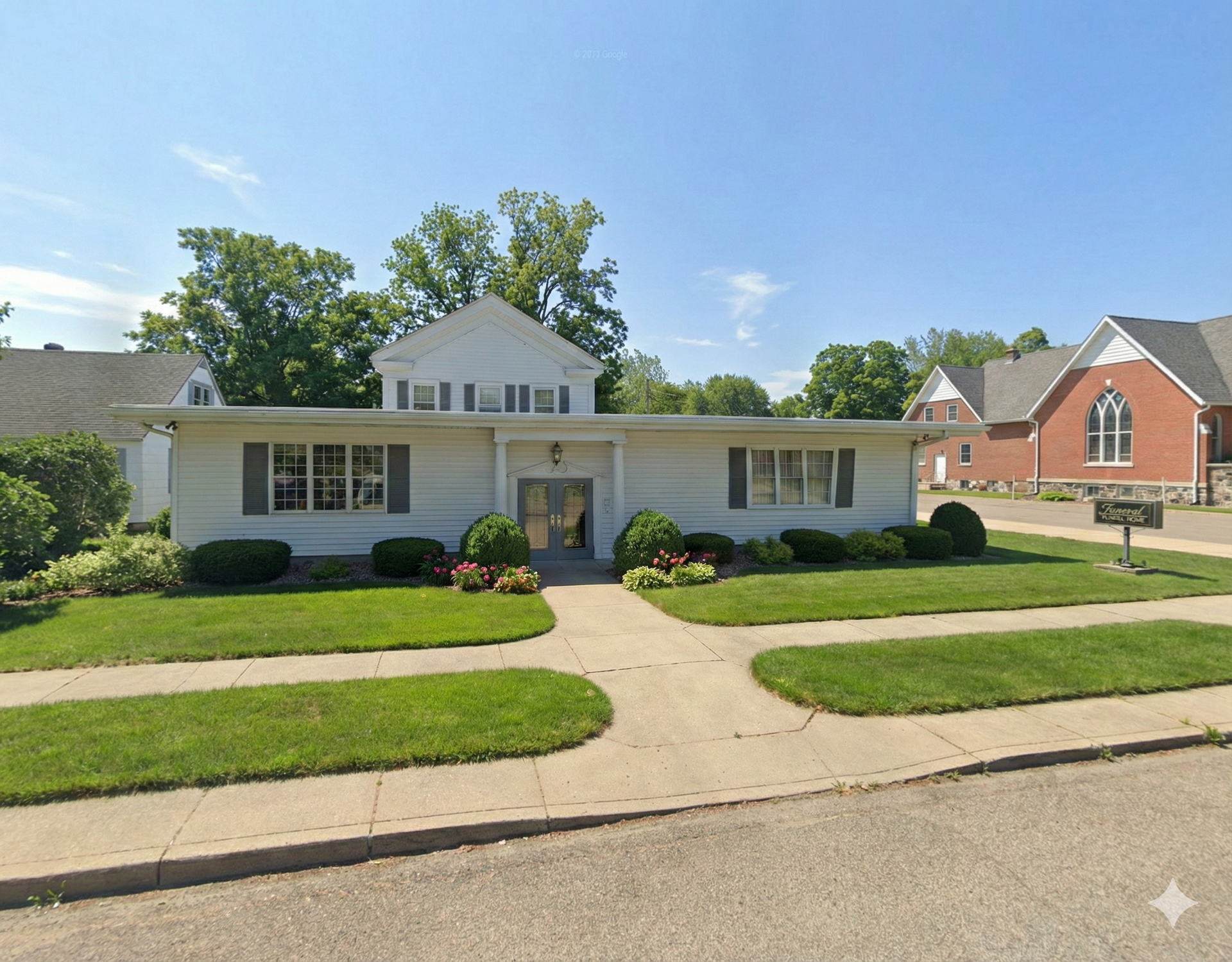Elegant home entrance with columns, wood door, topiary, and sconce lighting.