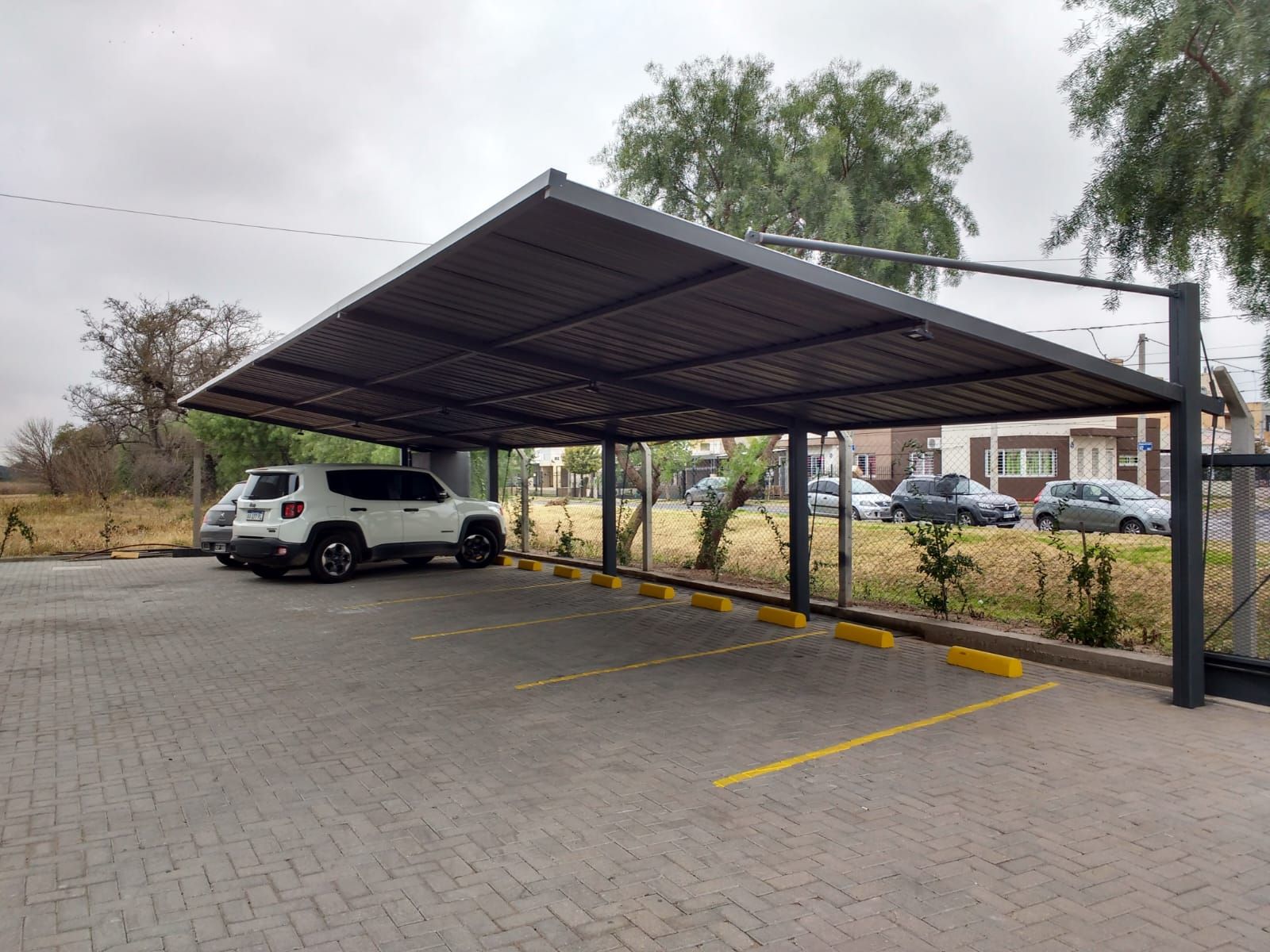 Estacionamiento techado con una camioneta SUV blanca estacionada bajo una marquesina metálica.