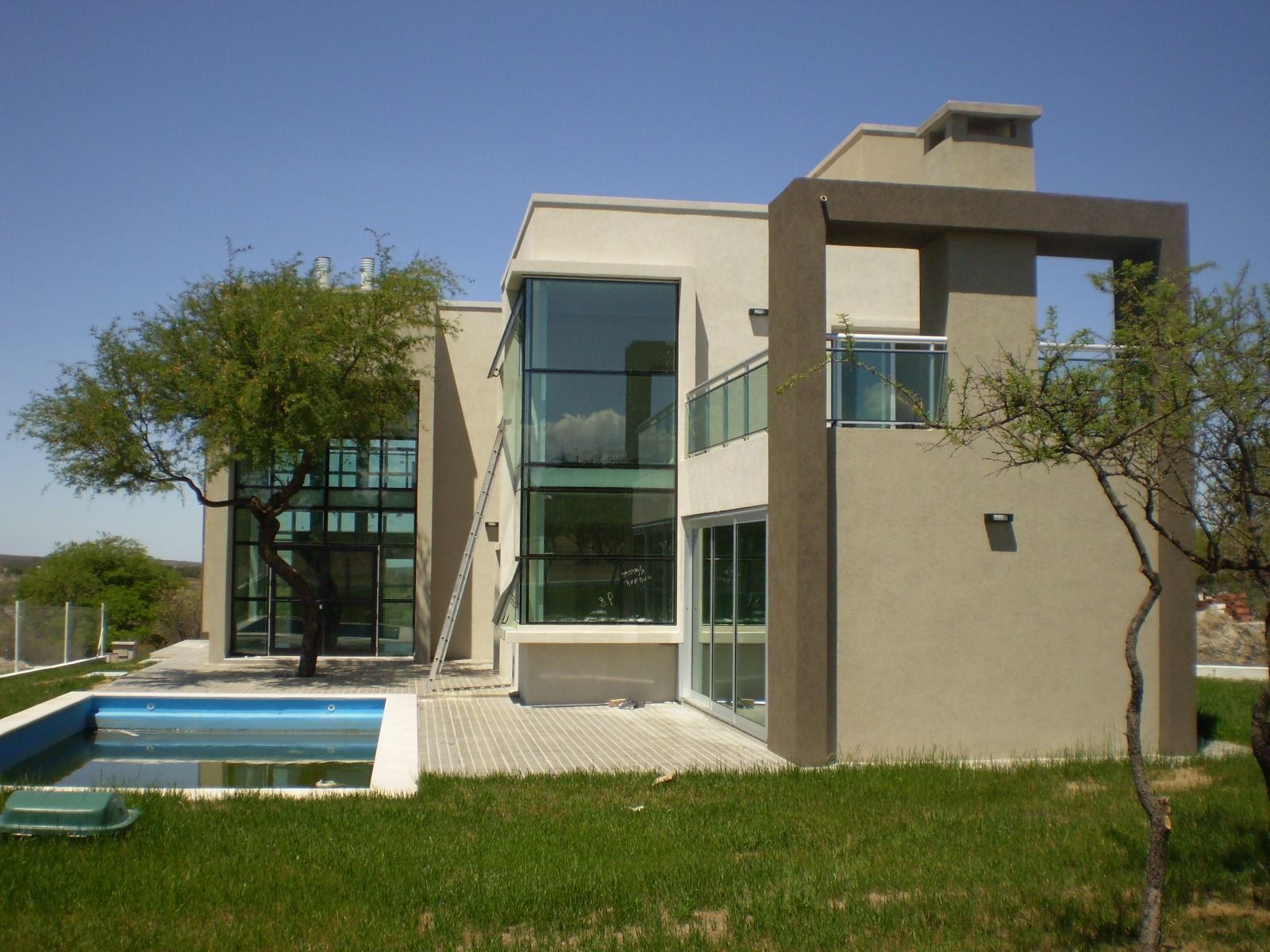 Casa moderna con balcones de cristal, piscina y césped verde bajo un cielo despejado.