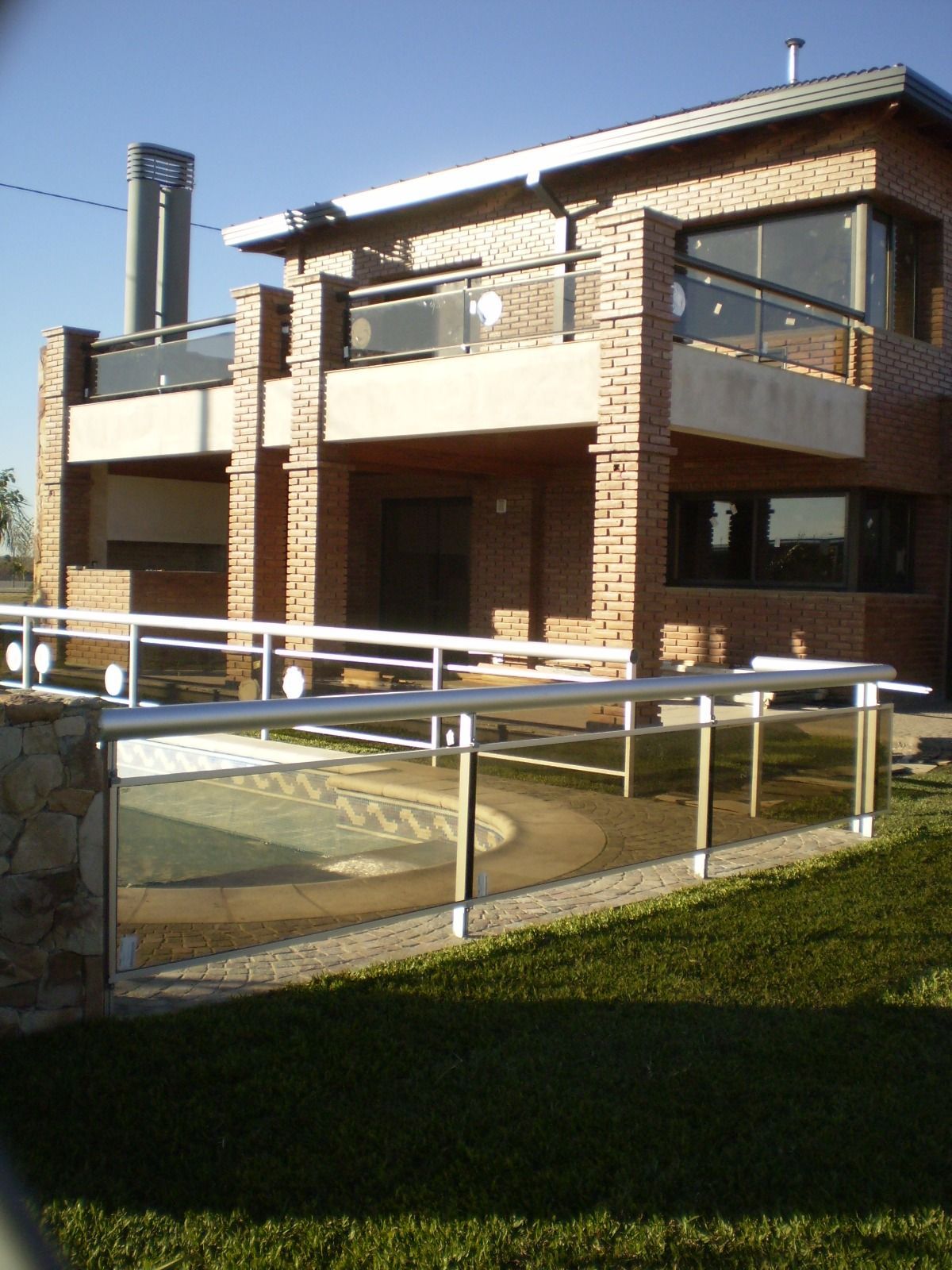 Casa de ladrillo de dos plantas con balcón y rampa de acceso para sillas de ruedas en un patio soleado.