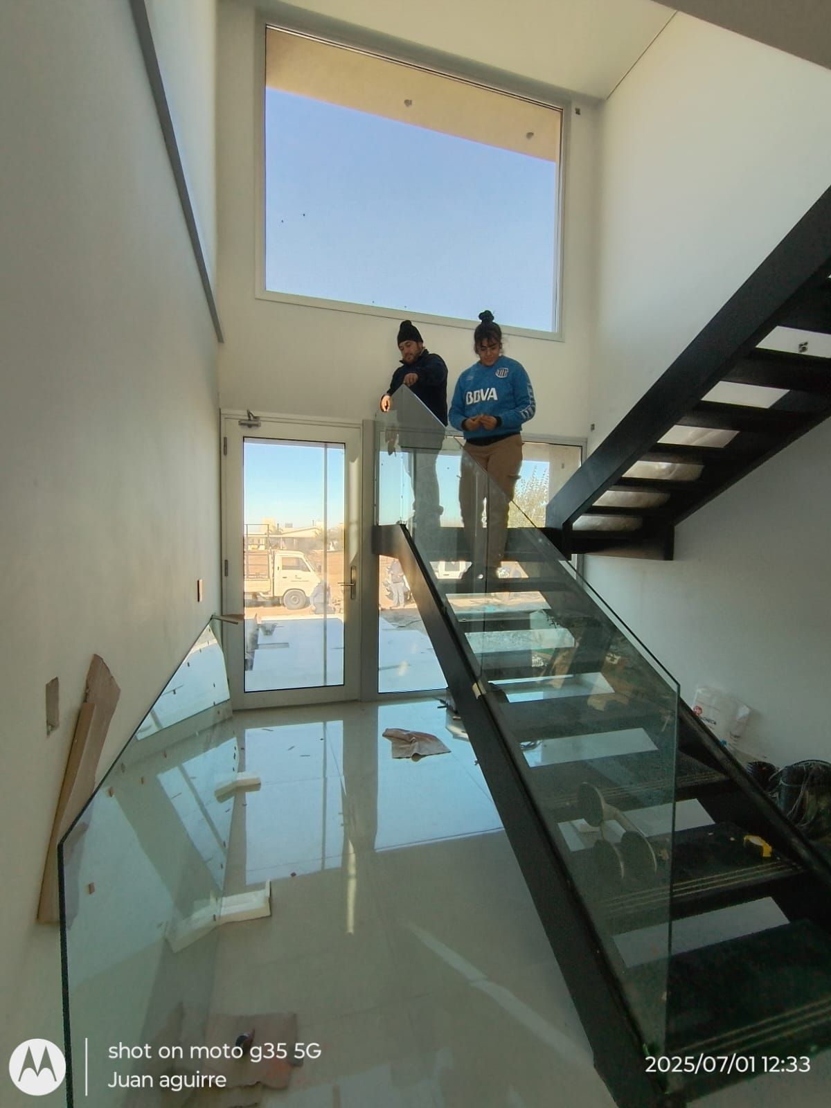 Dos personas de pie en una escalera de cristal en un interior moderno y luminoso.