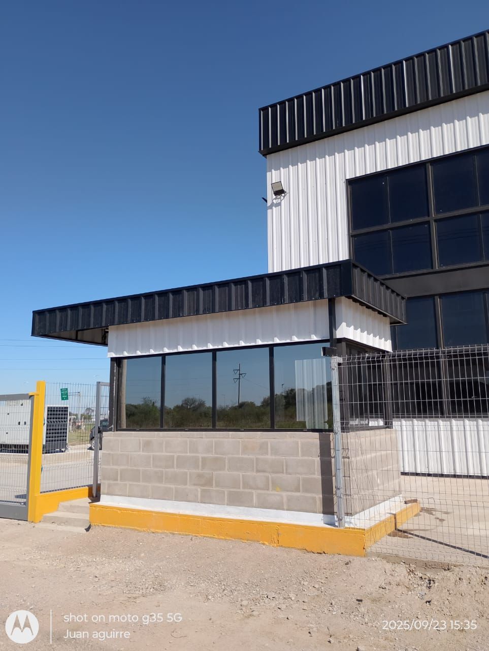 Entrada de edificio moderno con marquesina de acero, puertas de cristal y árboles al fondo.