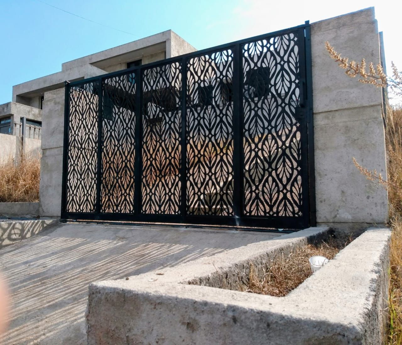 Entrada exterior cubierta junto a un edificio gris, con un patio pavimentado y una gran marquesina metálica.