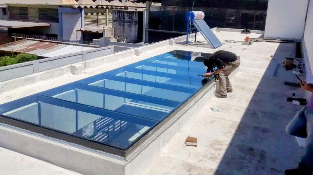 Un trabajador inspecciona una piscina rectangular en la azotea de un edificio, con agua azul y baldosas en el camino.