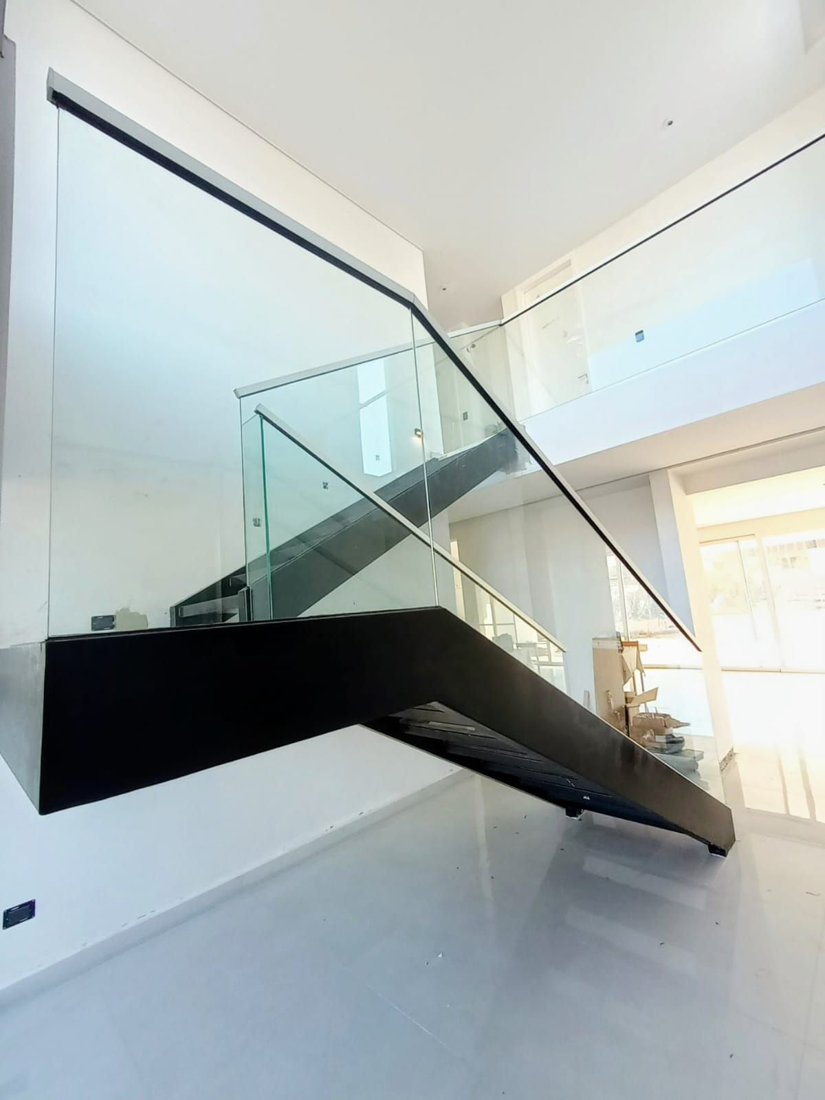 Escalera moderna con barandilla de cristal y parte inferior negra en un interior blanco brillante.