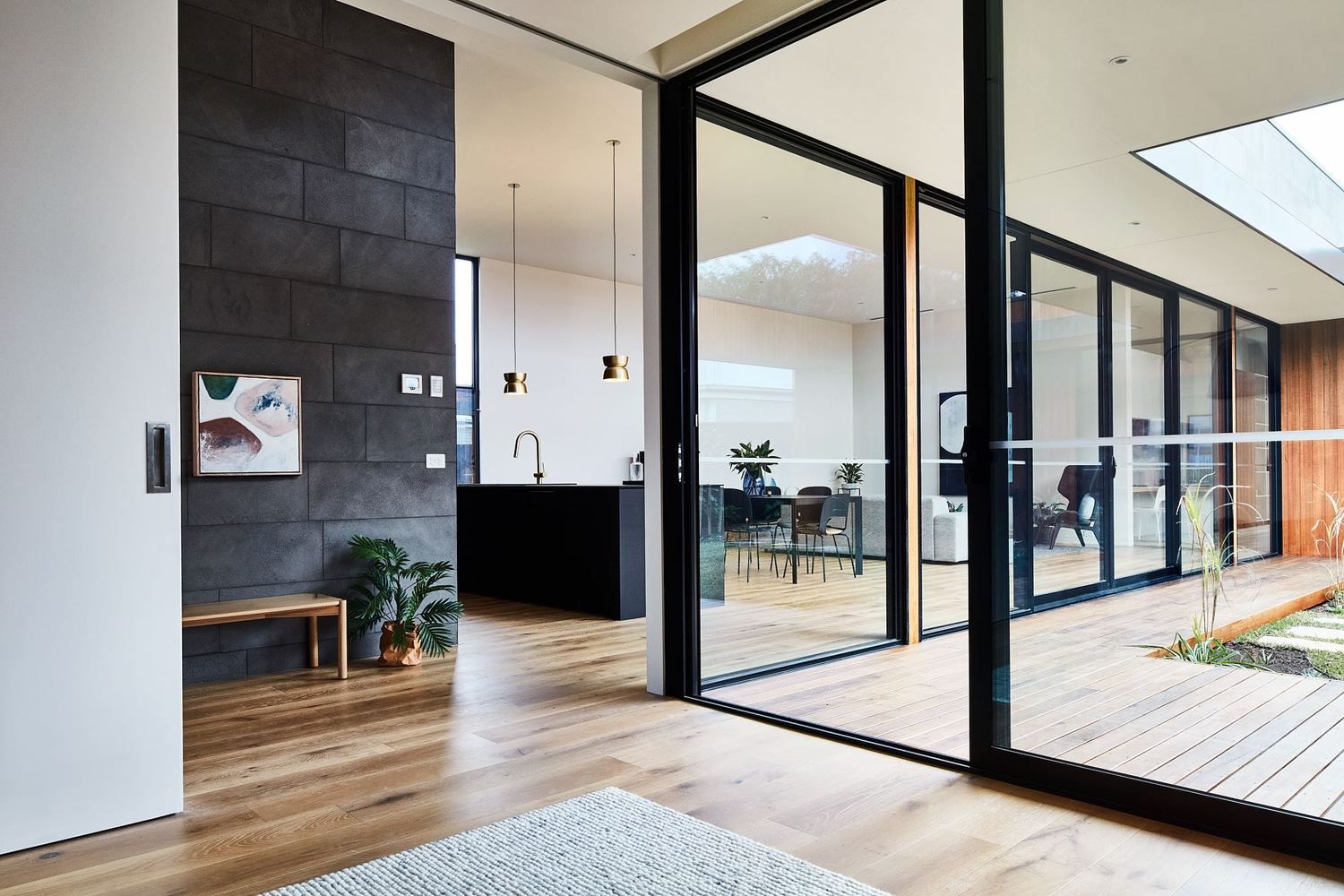 Espacio diáfano de estilo moderno con suelos de madera, puertas de cristal con marcos negros.