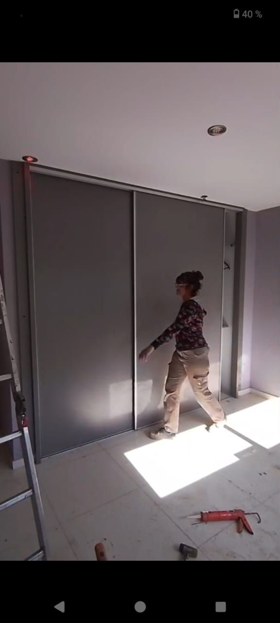 Una persona de pie en una habitación luminosa con puertas correderas grises en un armario y una herramienta roja en el suelo.