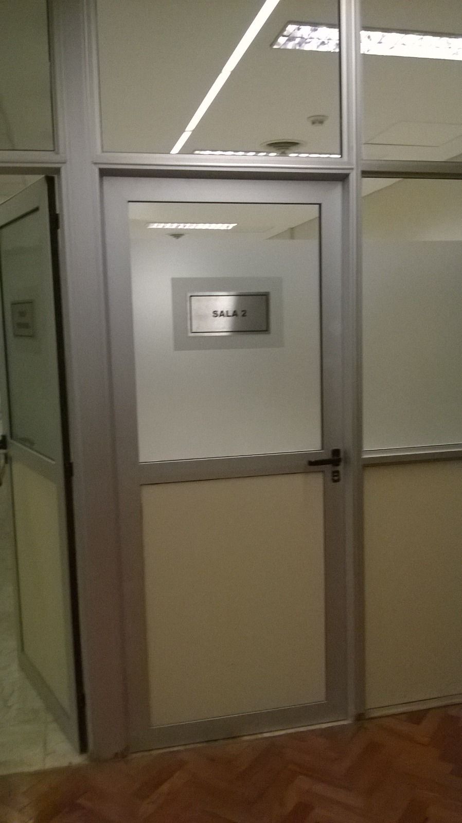 Puerta de oficina de cristal con panel inferior esmerilado y pared acristalada al lado.