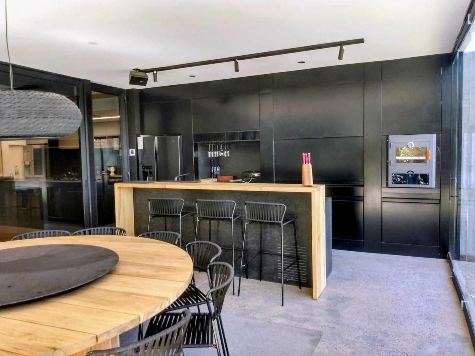 Cocina moderna con gabinetes negros, isla con encimera de madera, taburetes de bar y mesa de comedor redonda.