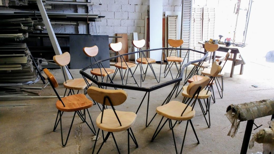 Una pila de sillas de metal alrededor de una mesa negra en un luminoso taller industrial.