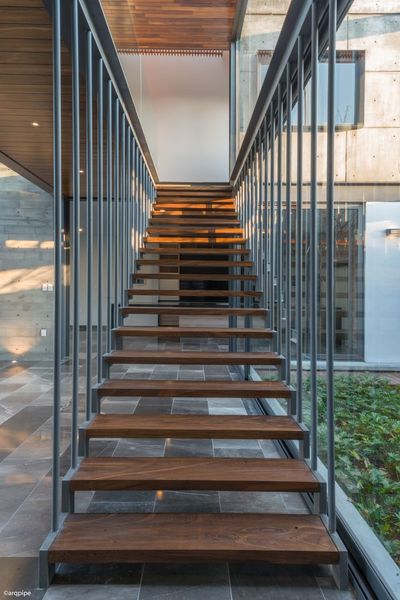 Escalera exterior moderna con peldaños de madera y barandillas de metal entre paredes de cristal.