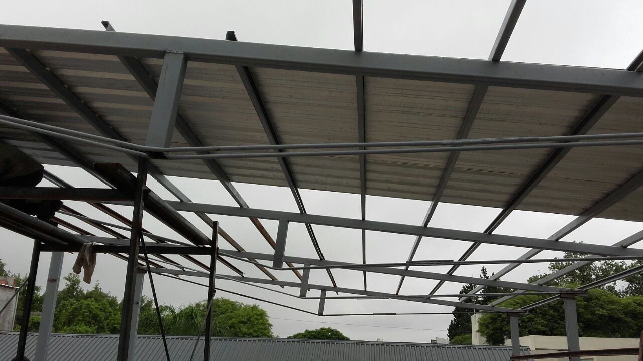 Estructura metálica cubierta para cochera con techo translúcido bajo un cielo nublado.