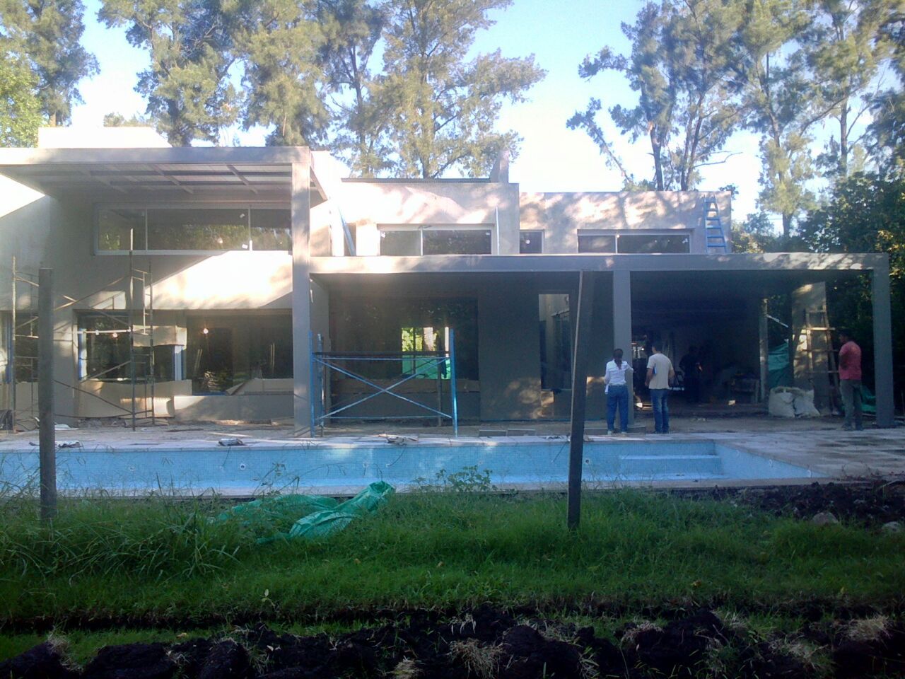 Edificio moderno con fachada de cristal, una piscina poco profunda y algunas personas de pie cerca de la entrada.