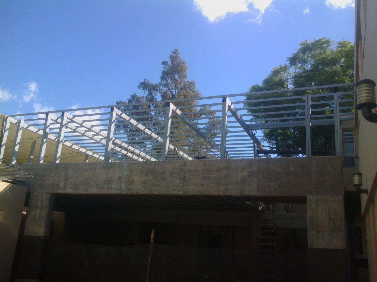 Pasarela al aire libre con barandillas metálicas sobre un paso subterráneo de hormigón bajo un cielo azul.