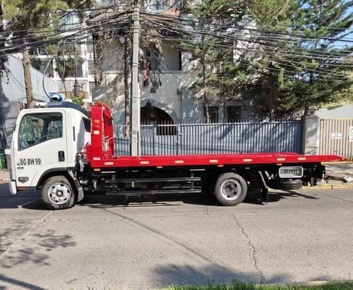 Una grúa blanca con plataforma roja está estacionada al costado de la carretera.