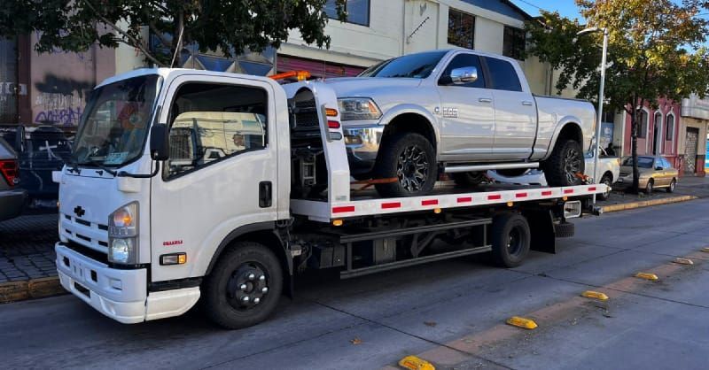Una grúa lleva un camión plateado en la parte trasera.