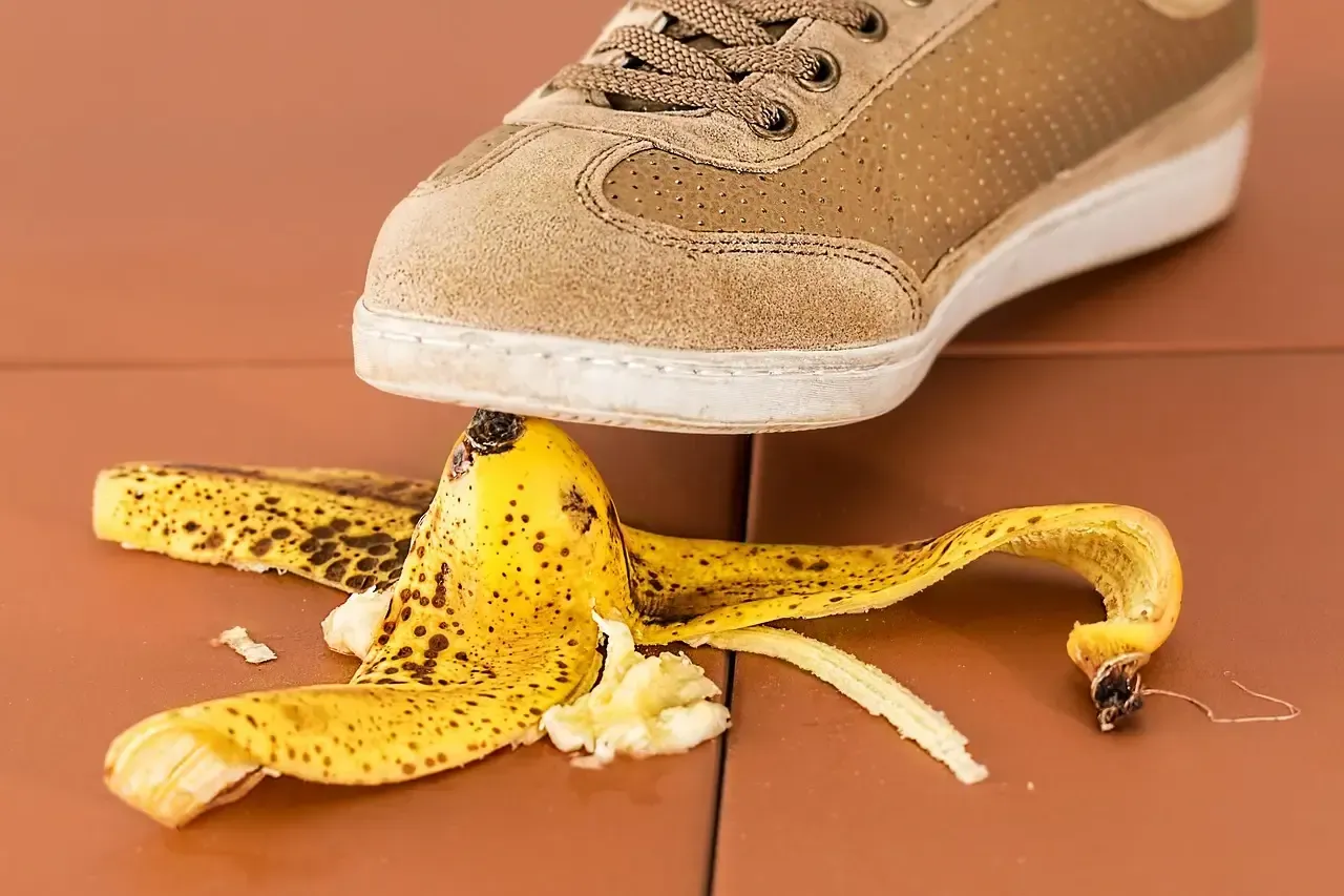 Beige shoe stepping on a yellow banana peel on a brown tiled floor.