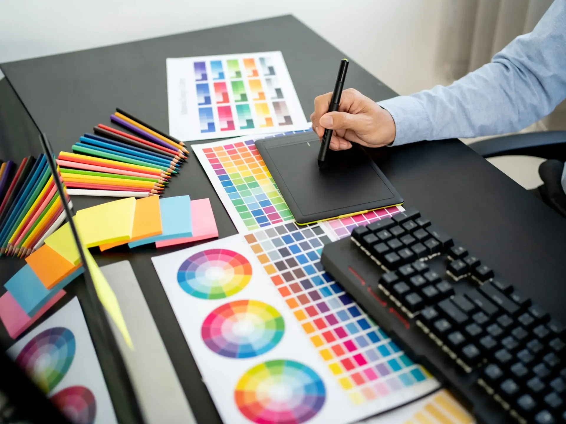 Person using a stylus on a drawing tablet, surrounded by color swatches and a keyboard.