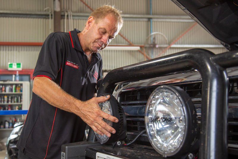 Auto electrician working in a workshop, adjusting spotlights on the front of a vehicle
