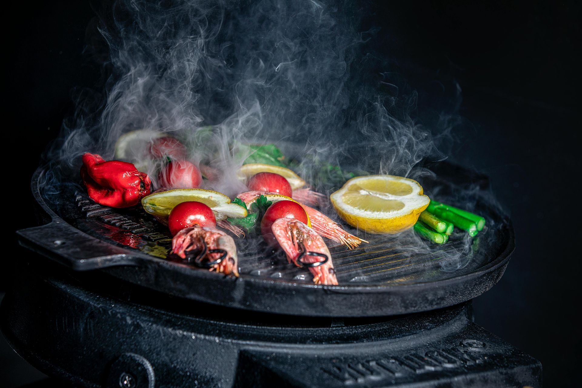 Grill with steaming seafood and vegetables: peppers, tomatoes, and lemon slices.