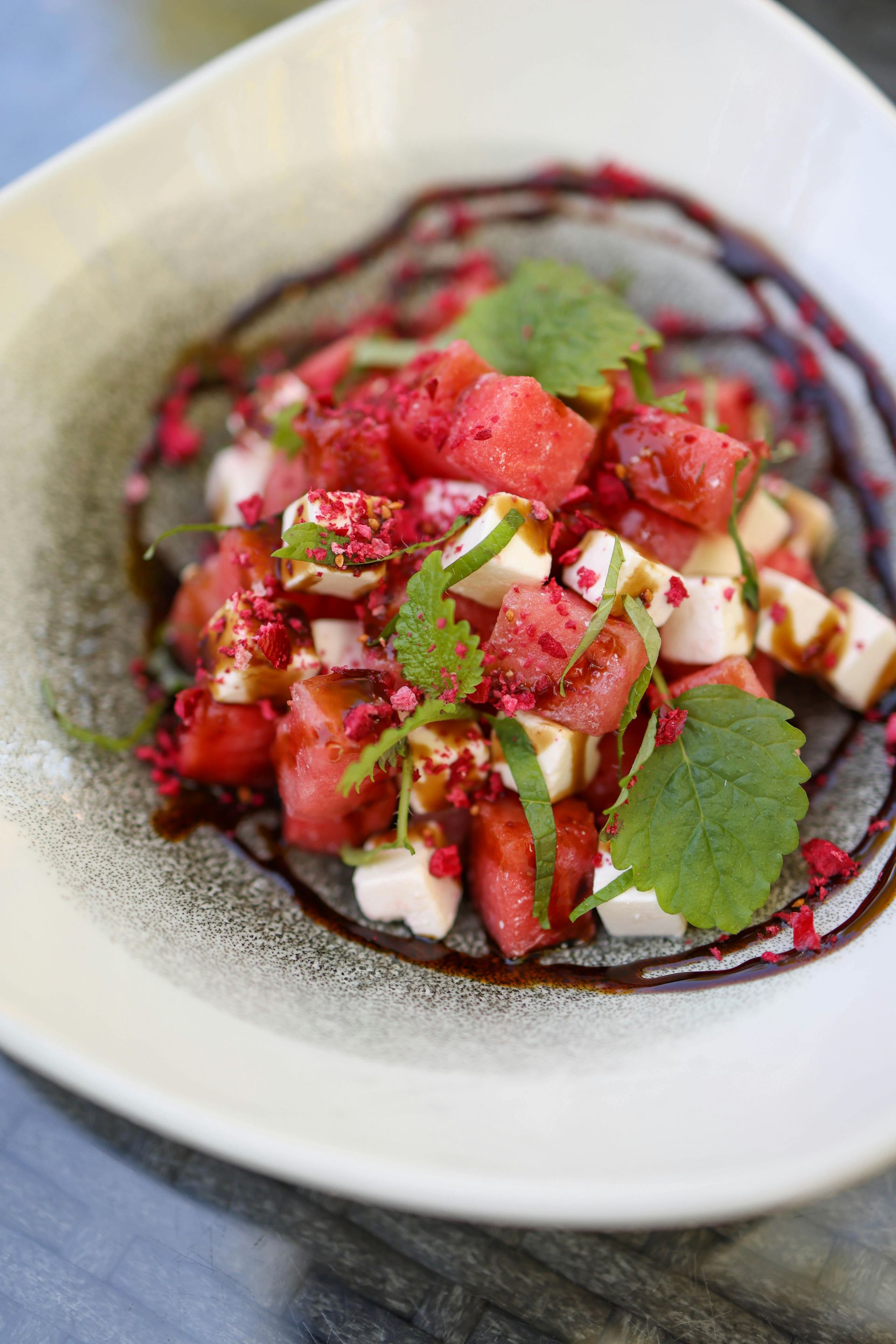 Watermelon and feta salad with balsamic glaze and mint leaves in a white bowl.