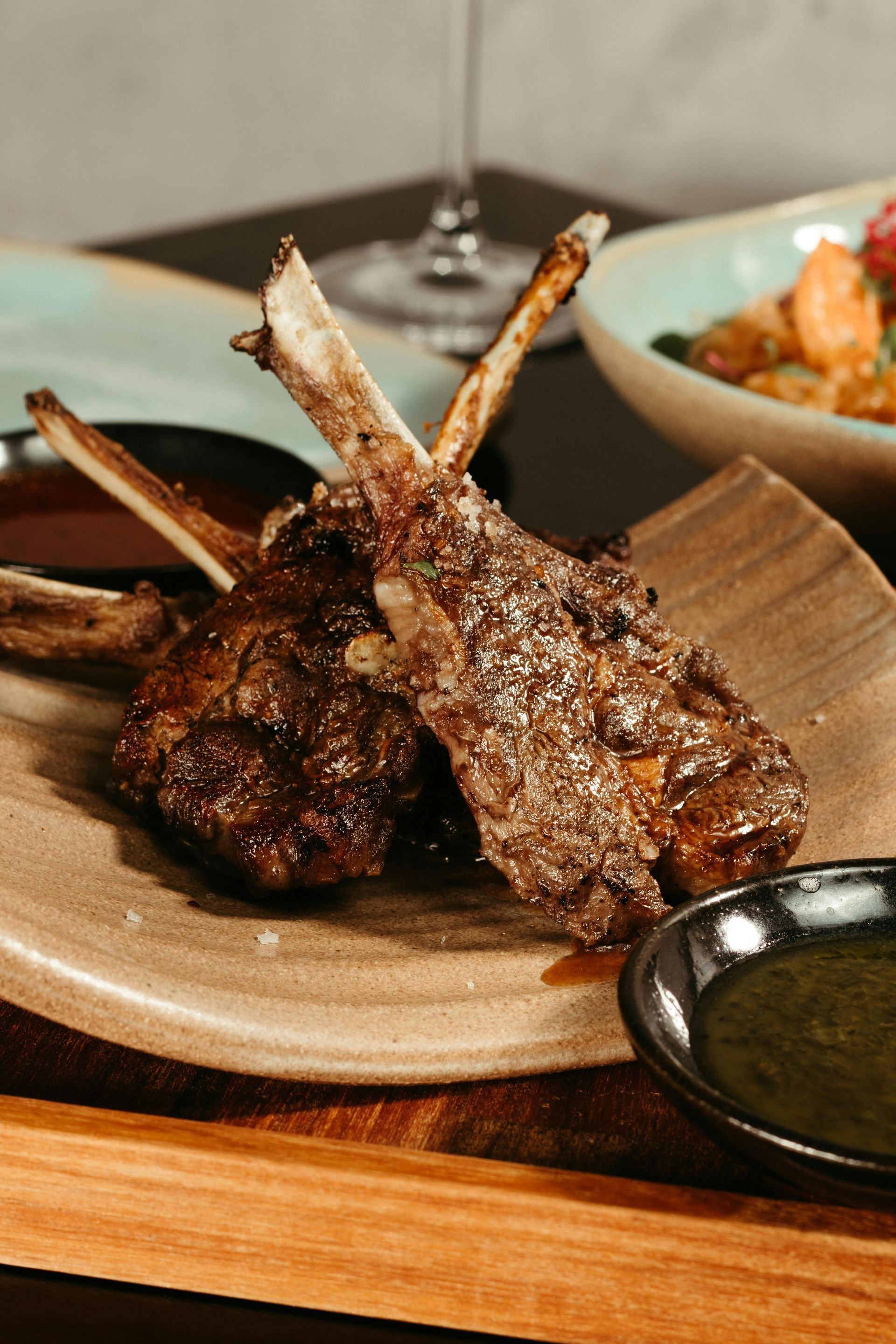 Grilled lamb chops on a plate with dipping sauce and a side dish.