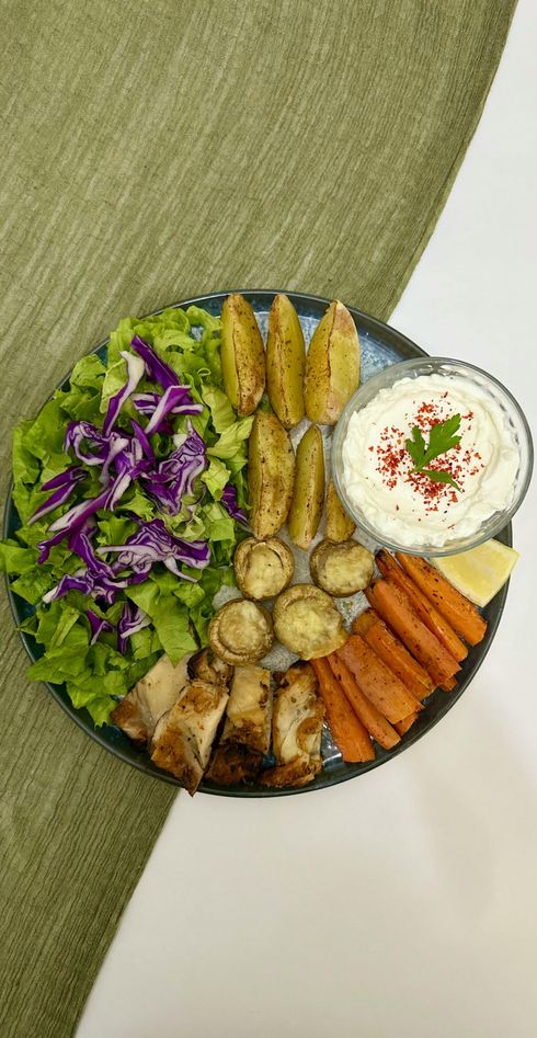 Plate with roasted chicken, potatoes, mushrooms, carrots, salad, and dip.