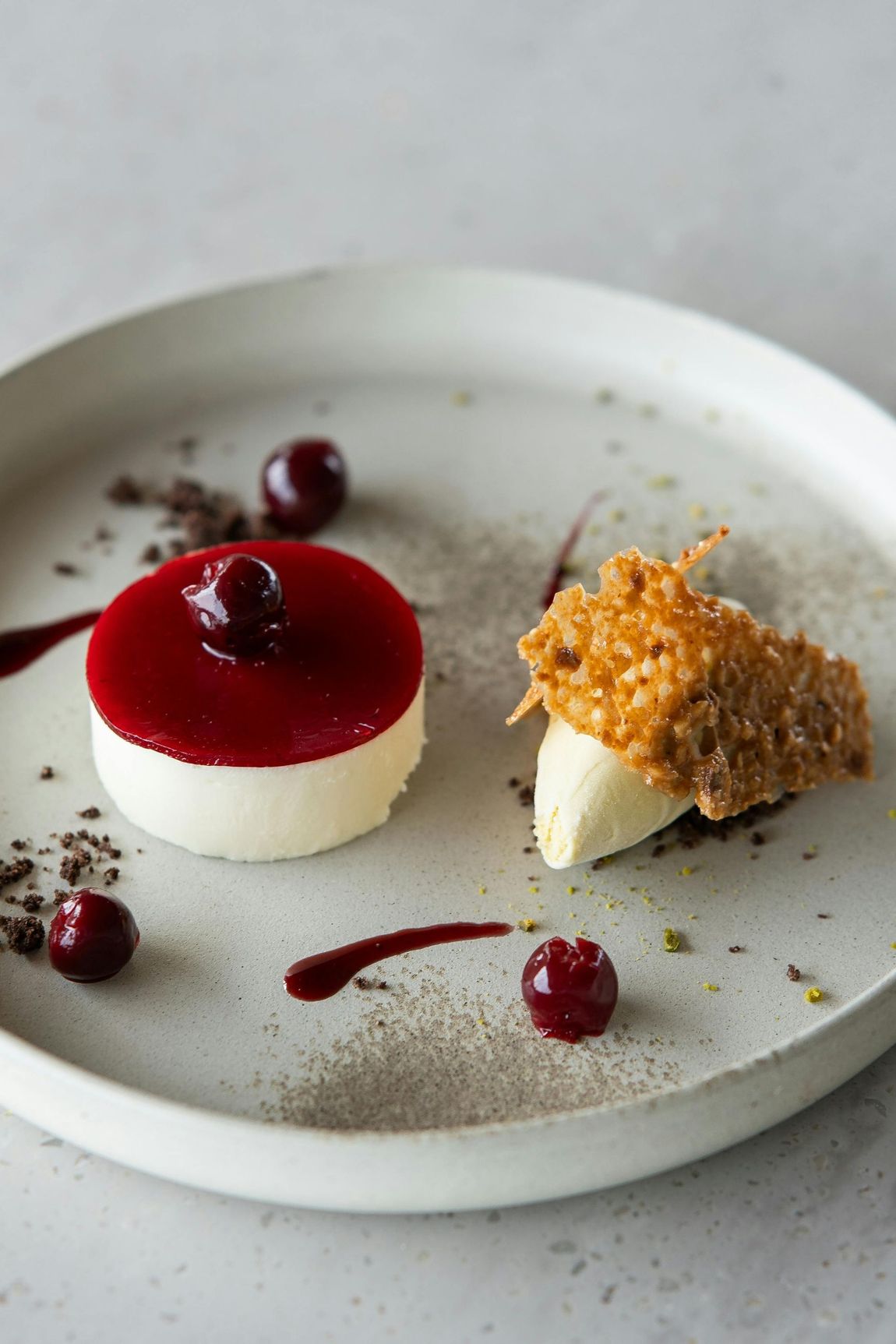 Dessert on plate: white mousse with cherry topping, caramel crisp, and fresh cherries.