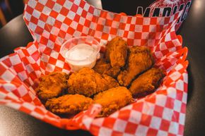 Fried chicken wings with dipping sauce in a red and white checkered basket.
