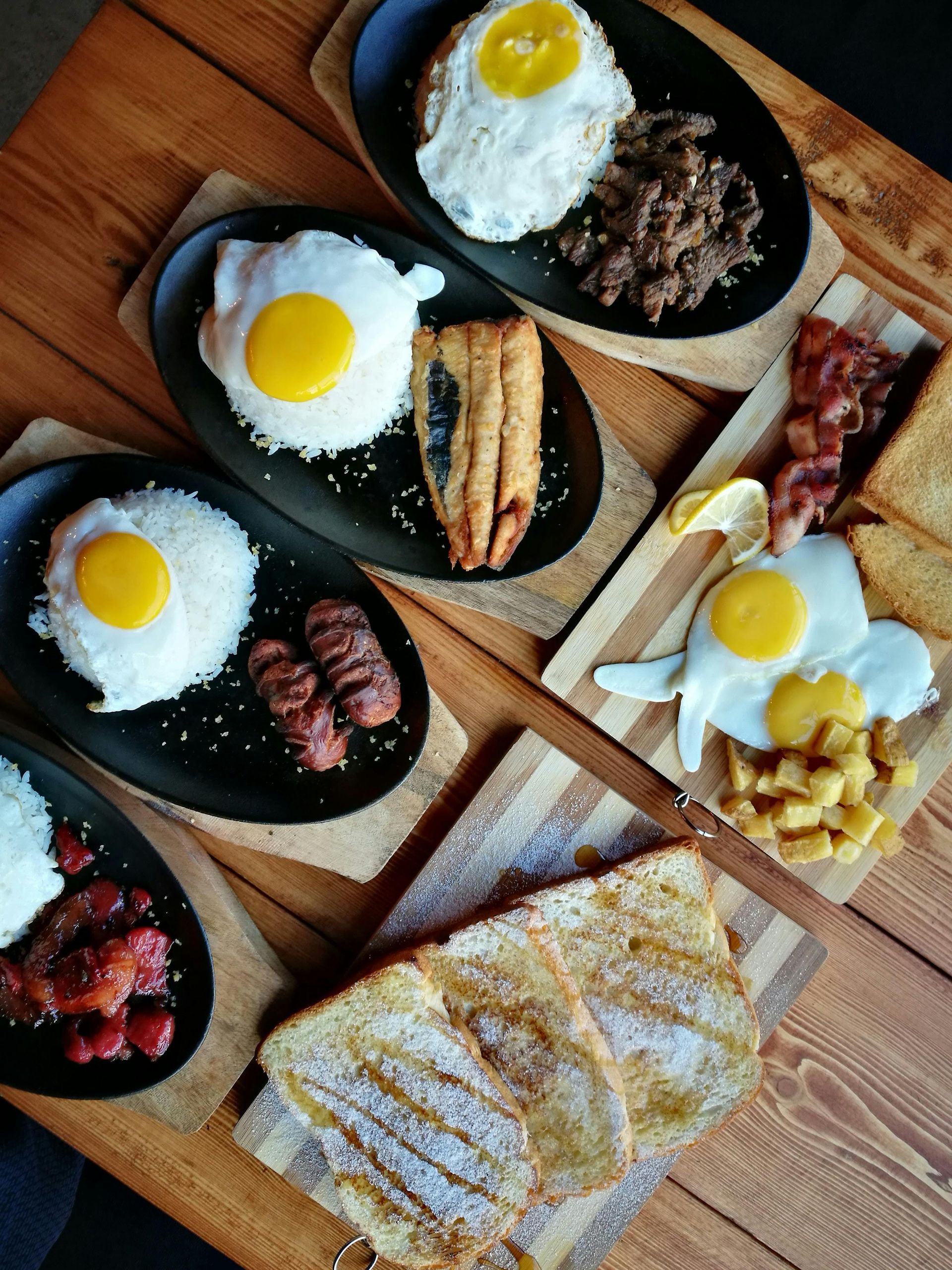 Breakfast spread: Eggs, rice, meats, and toast on wooden platters, served on a wood table.