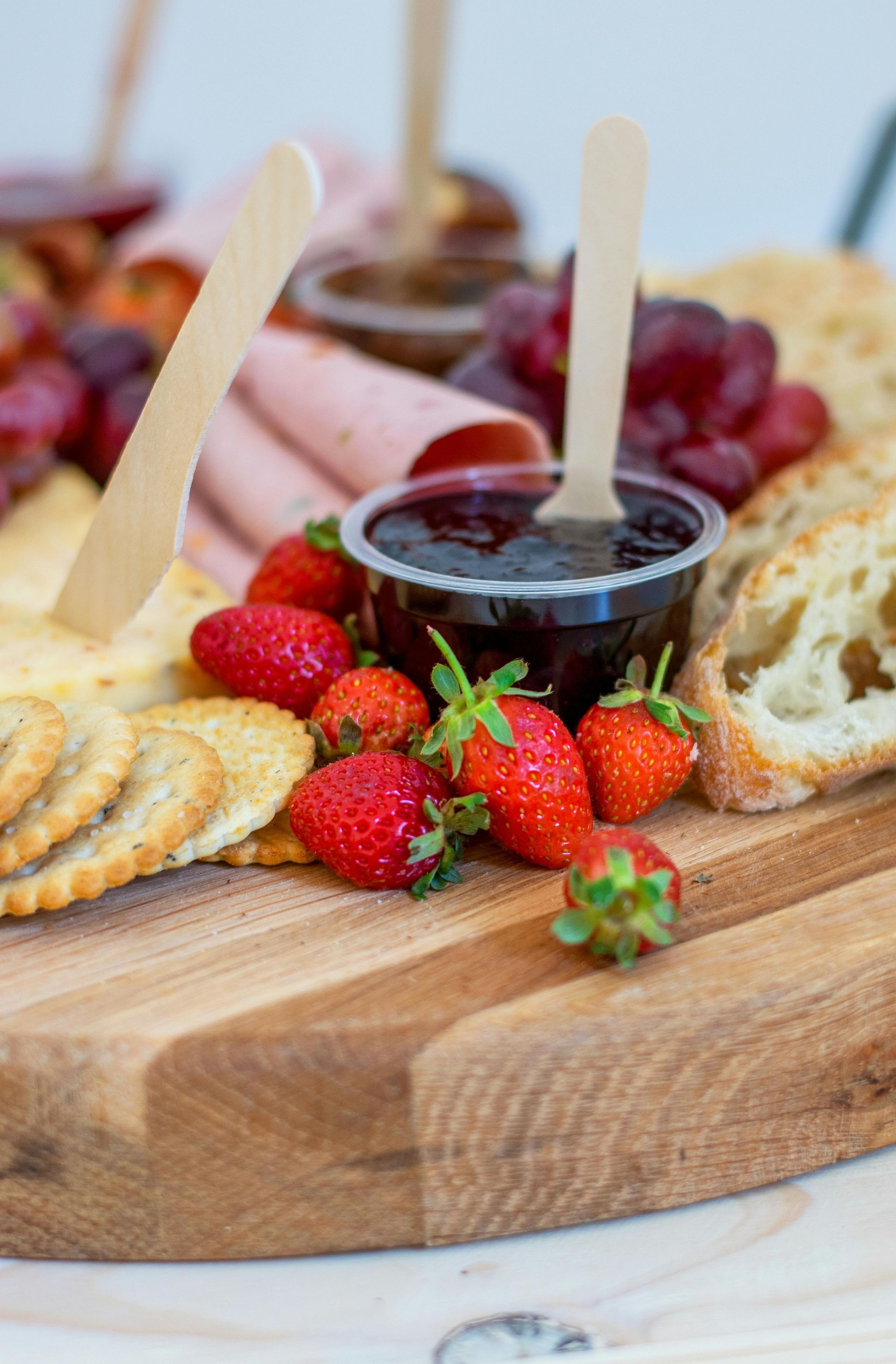Charcuterie board with crackers, strawberries, jam, grapes, bread, and salami.