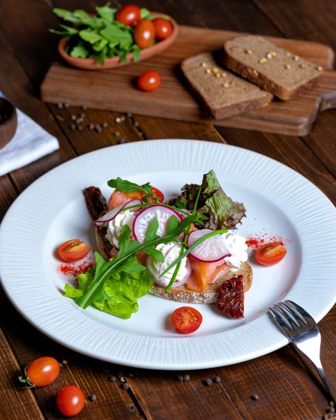 Smoked salmon and cream cheese toast with radish, arugula, and cherry tomatoes on a white plate.