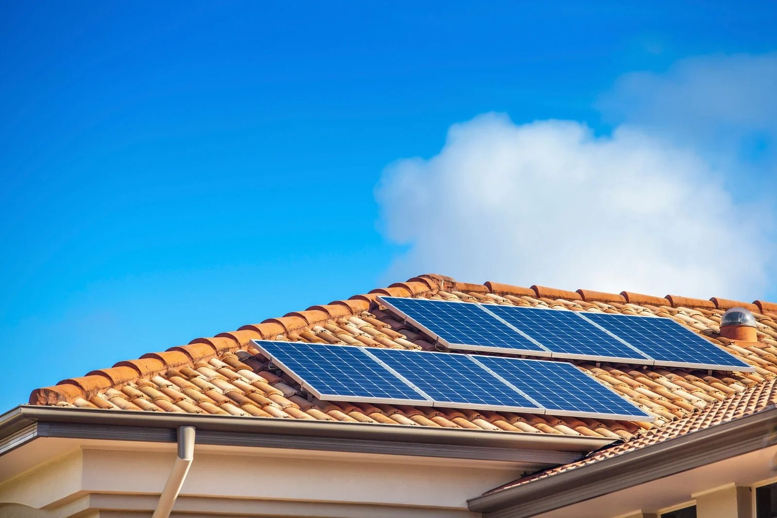 Solar panels on a terracotta roof under a bright blue sky with clouds