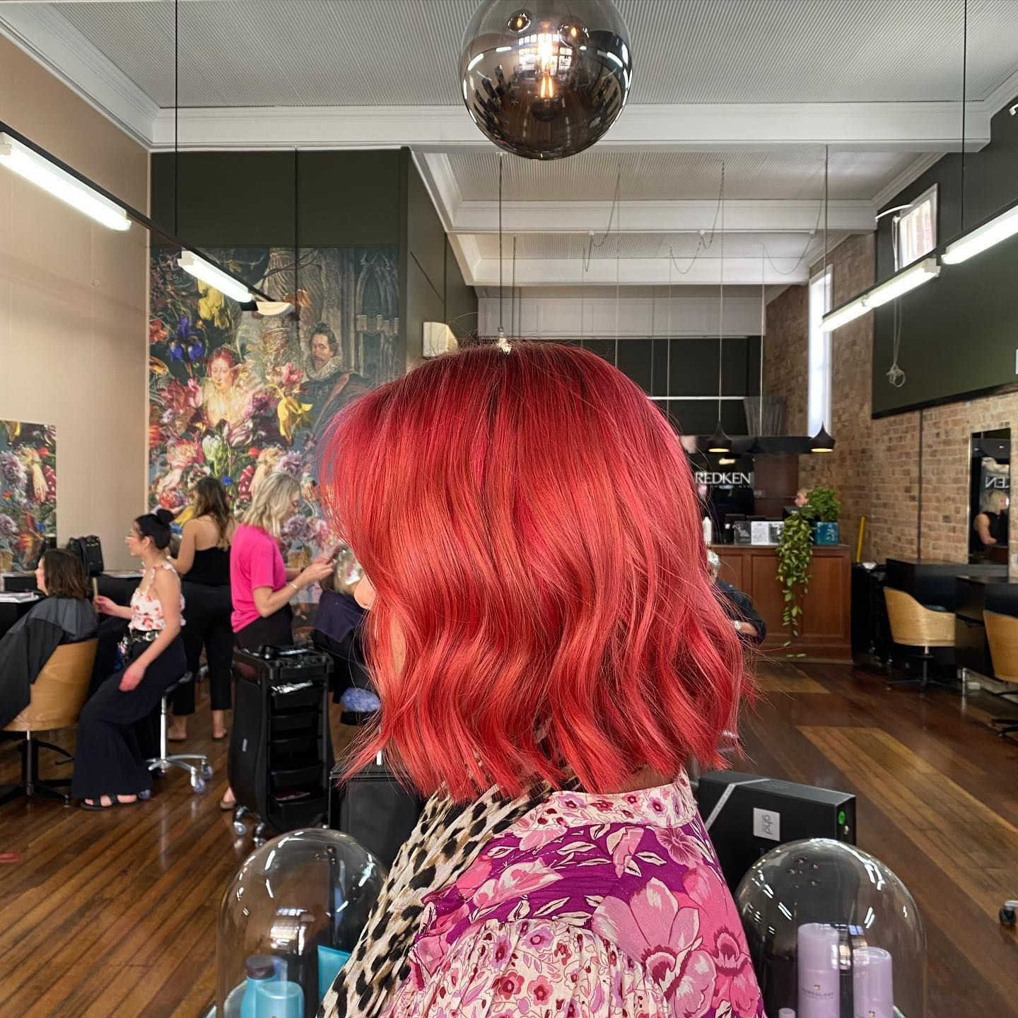 Woman with bright red wavy hair in a hair salon. Other people and a disco ball are visible.