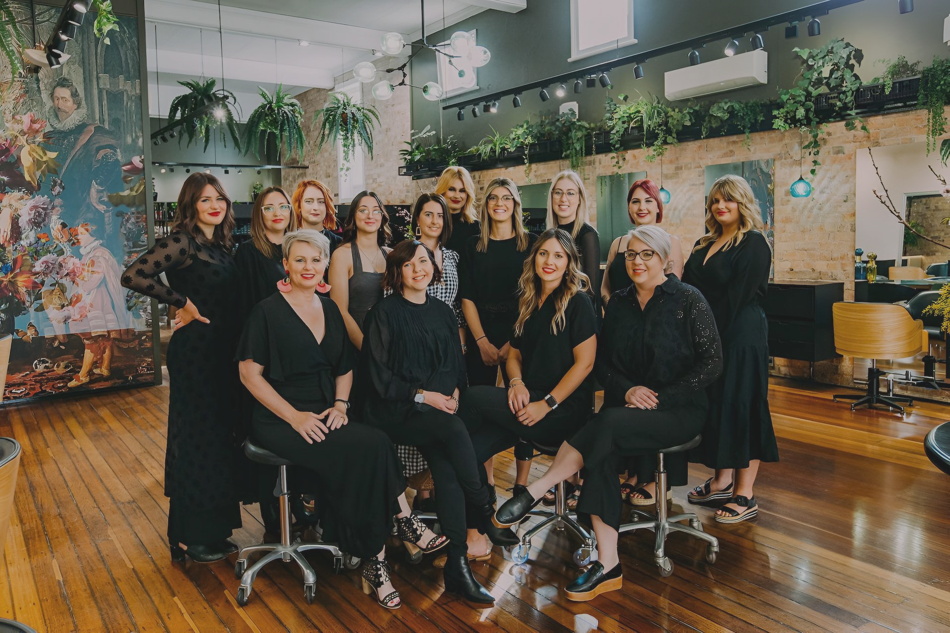 Group of women, hairdressers, in a salon setting. They are wearing black and smiling.