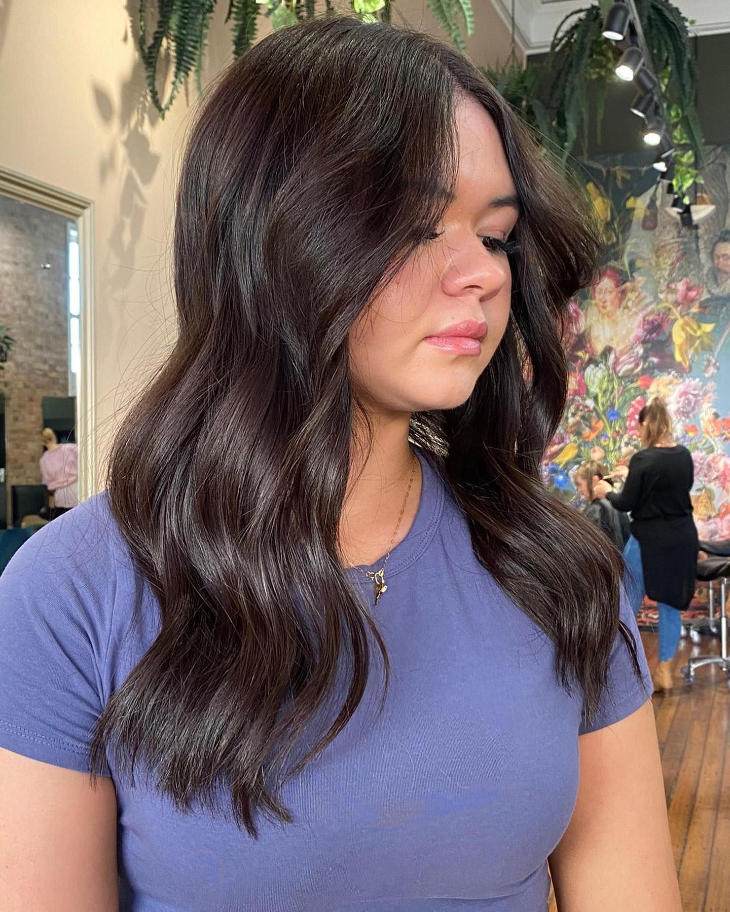 Woman with dark wavy hair, wearing a blue shirt, inside a salon.
