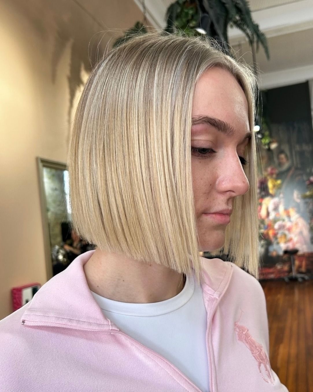 Blonde woman with angled bob hairstyle, wearing pink zip-up, looking right.