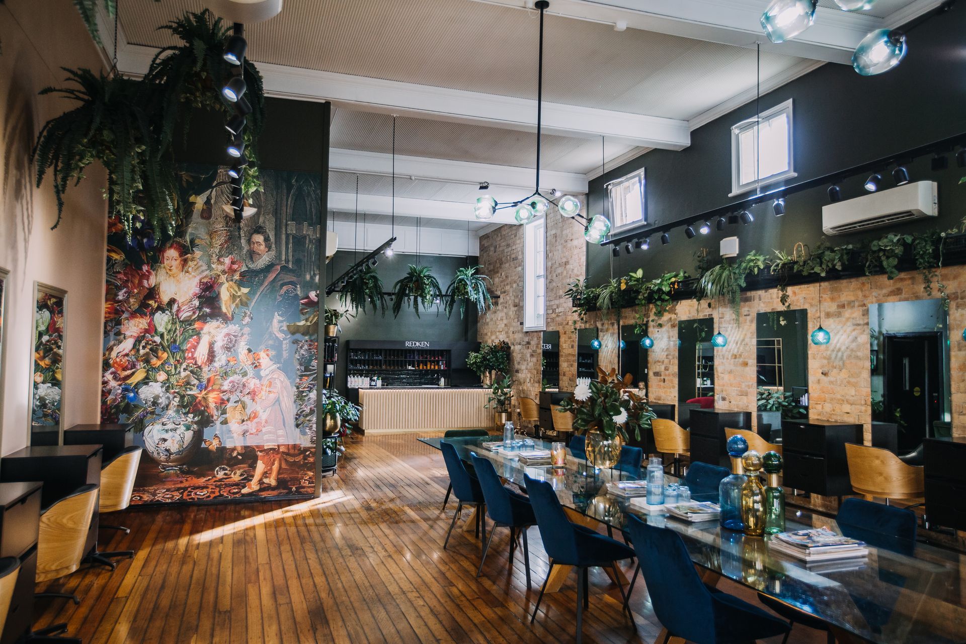 Hair salon interior with long table, chairs, mirrors, and floral mural.