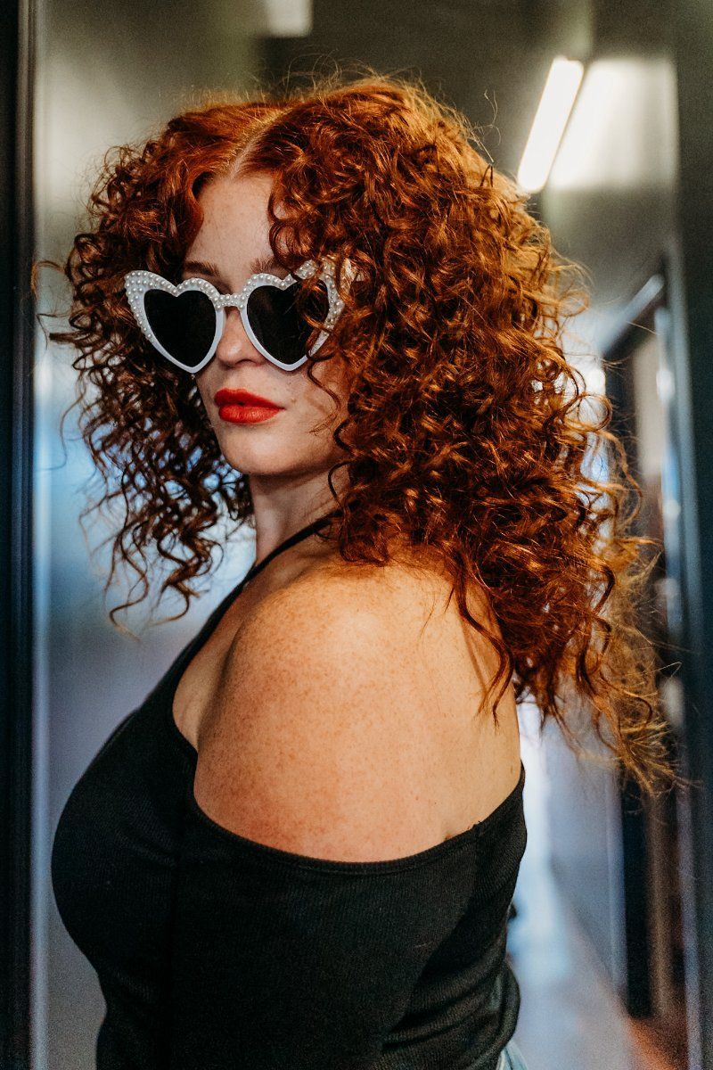 A Woman With Curly Red Hair is Wearing Heart Shaped Sunglasses — Air Hair Studio in Toowoomba City, QLD