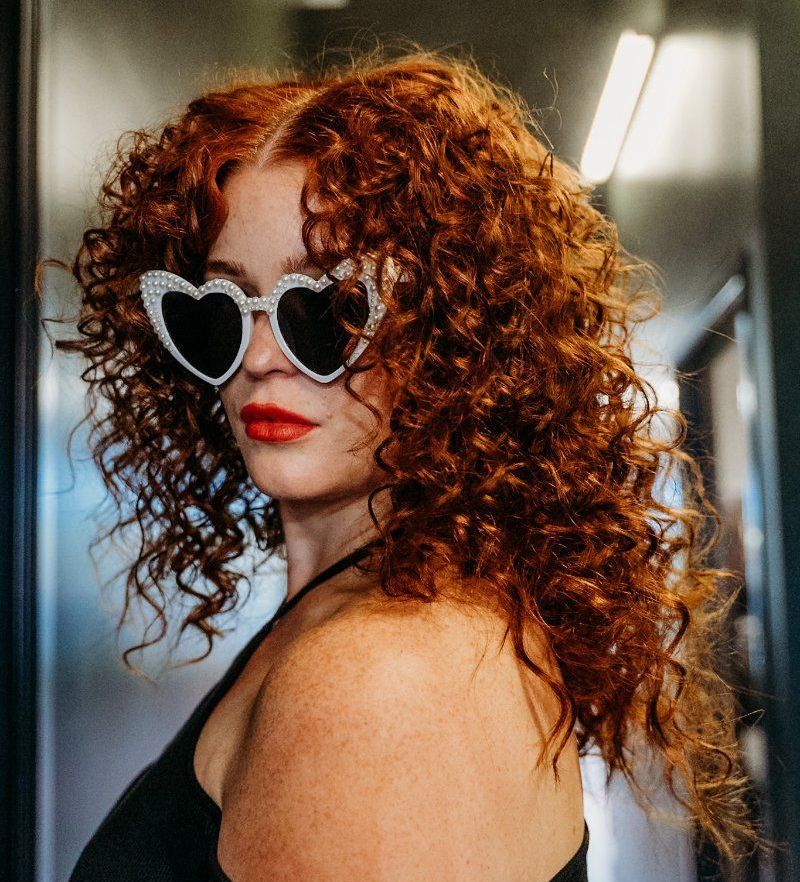 A woman with curly hair wearing heart shaped sunglasses