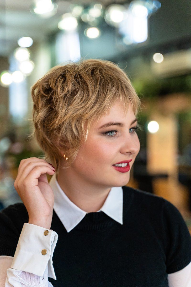A woman with short blonde hair is wearing a black shirt and white collar.