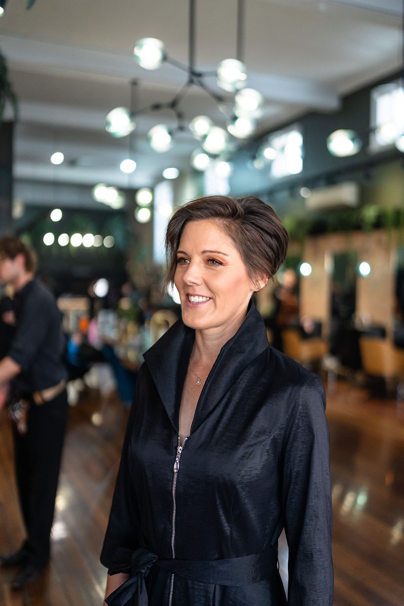 A woman with short hair is smiling and wearing a black jacket.