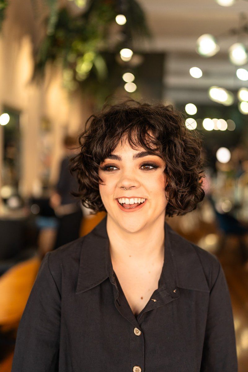 A Woman With Curly Hair is Smiling in a Salon — Air Hair Studio in Toowoomba City, QLD