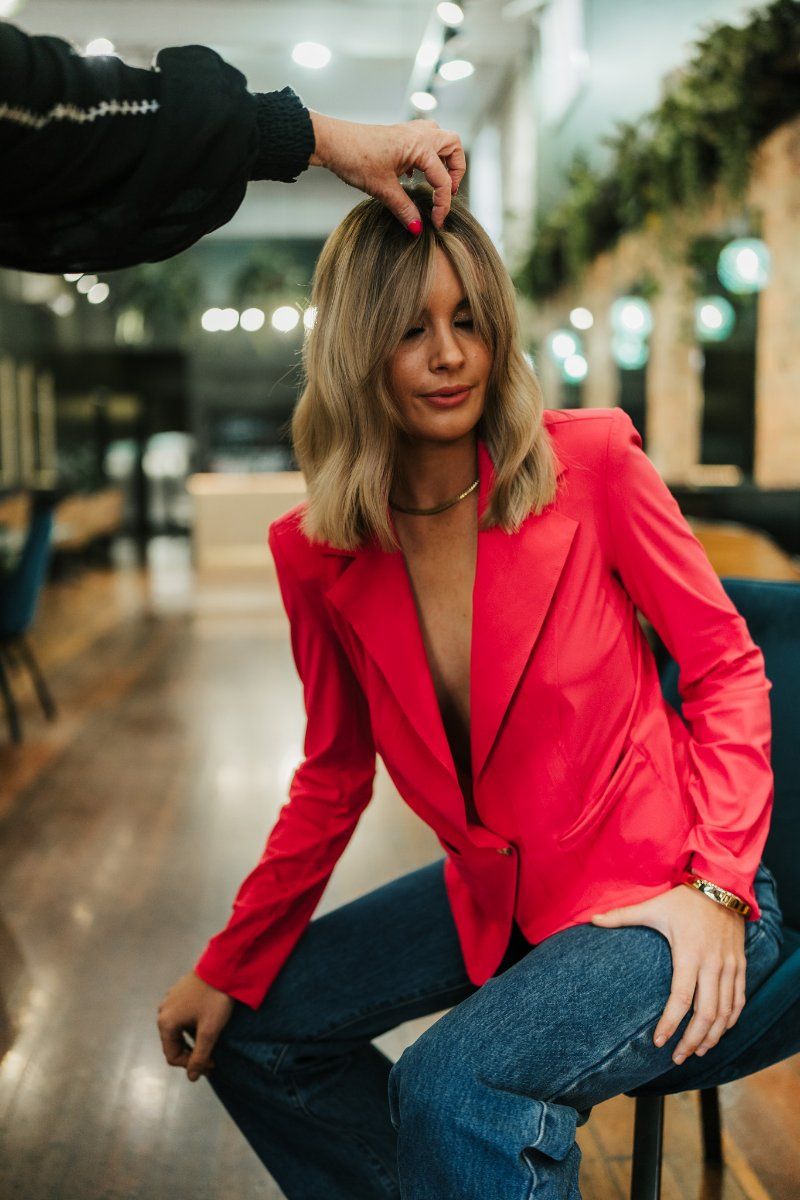 A Woman in a Red Jacket is Sitting on a Chair Getting Her Hair Cut — Air Hair Studio in Toowoomba City, QLD