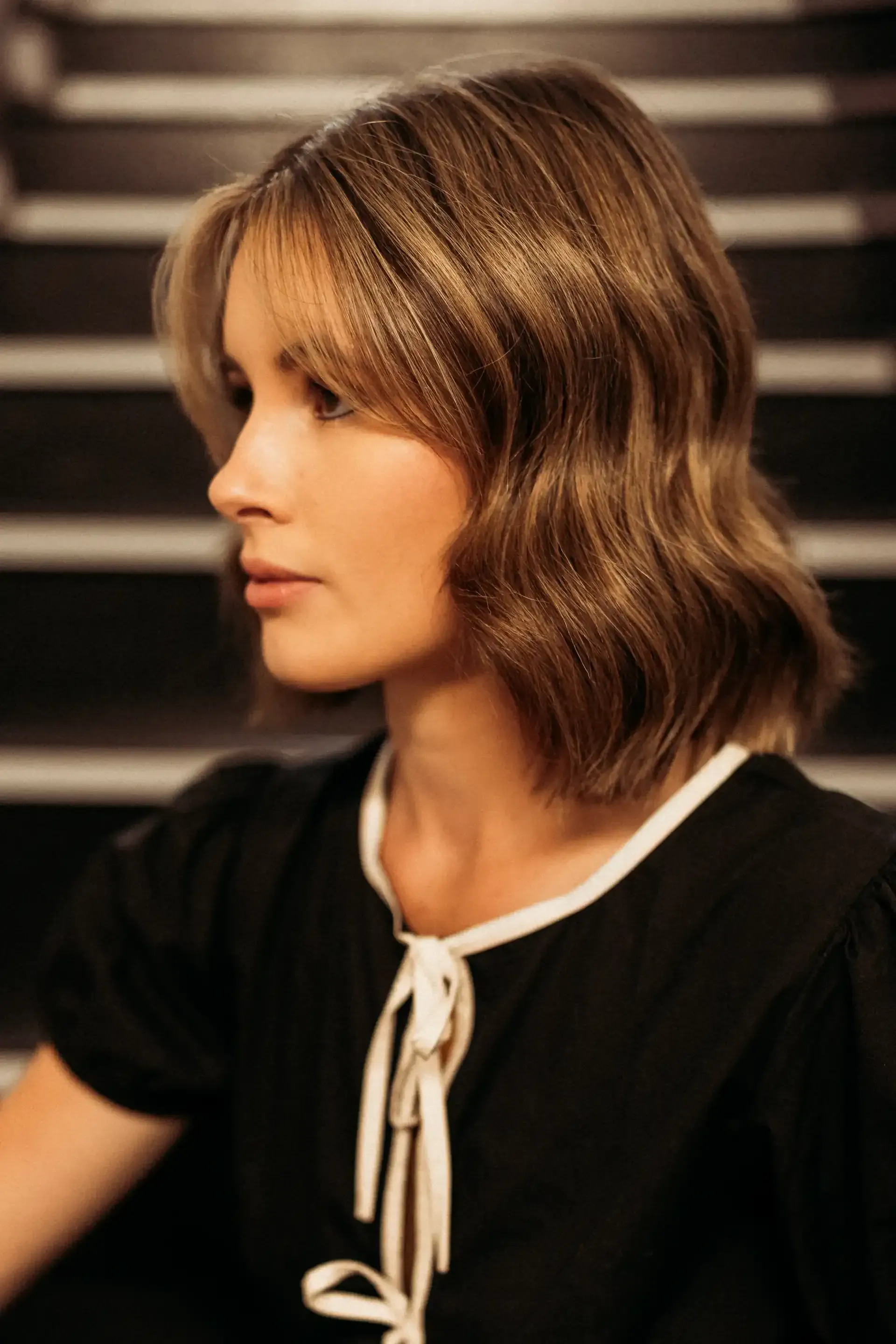 A woman with short brown hair is wearing a black dress and sitting on a set of stairs.