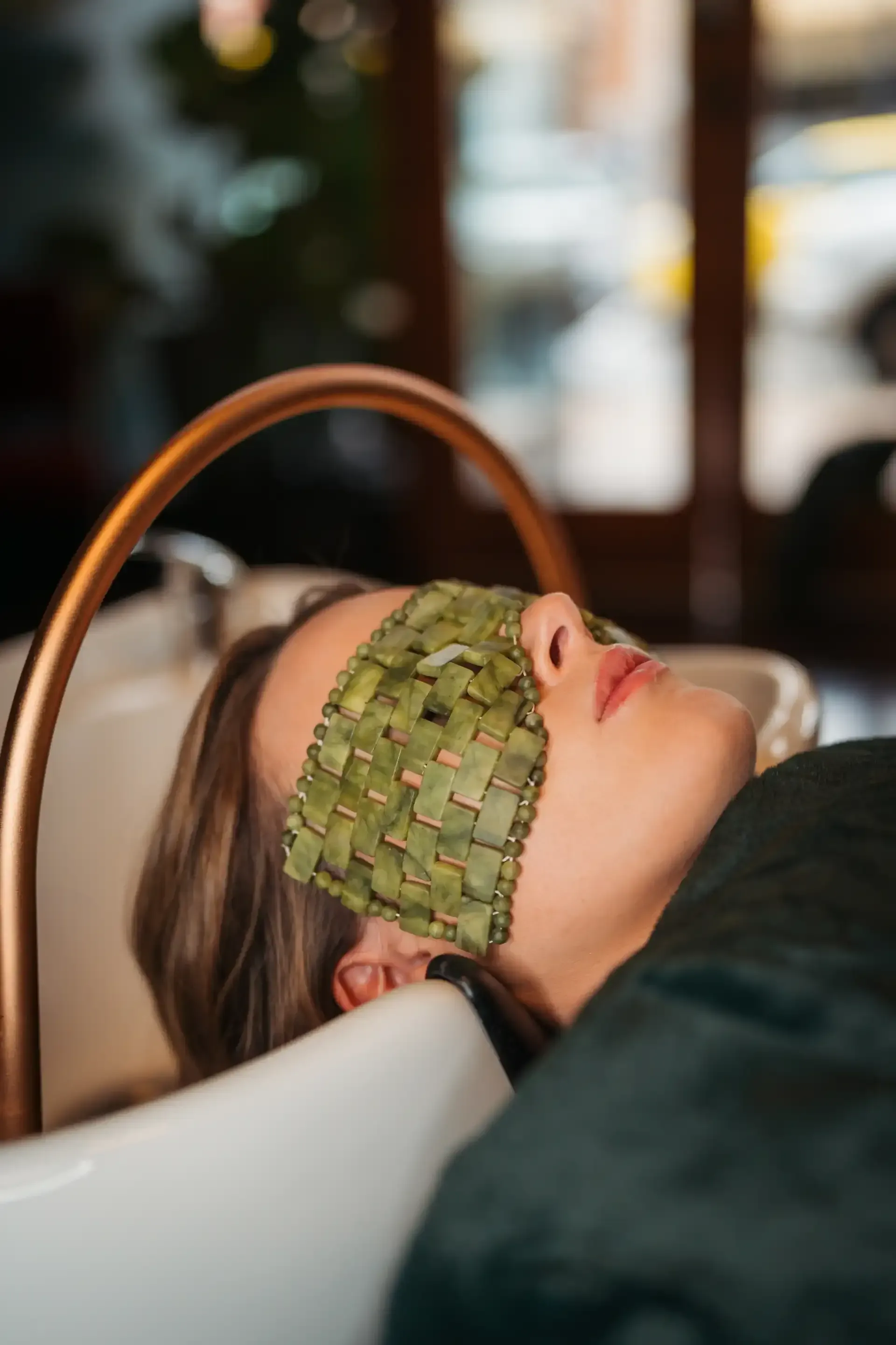 A woman is laying in a sink with a green mask on her face.