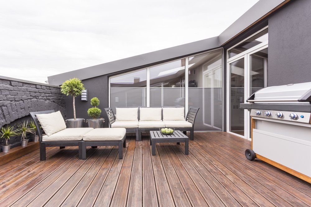 A wooden deck with furniture and a grill on it.