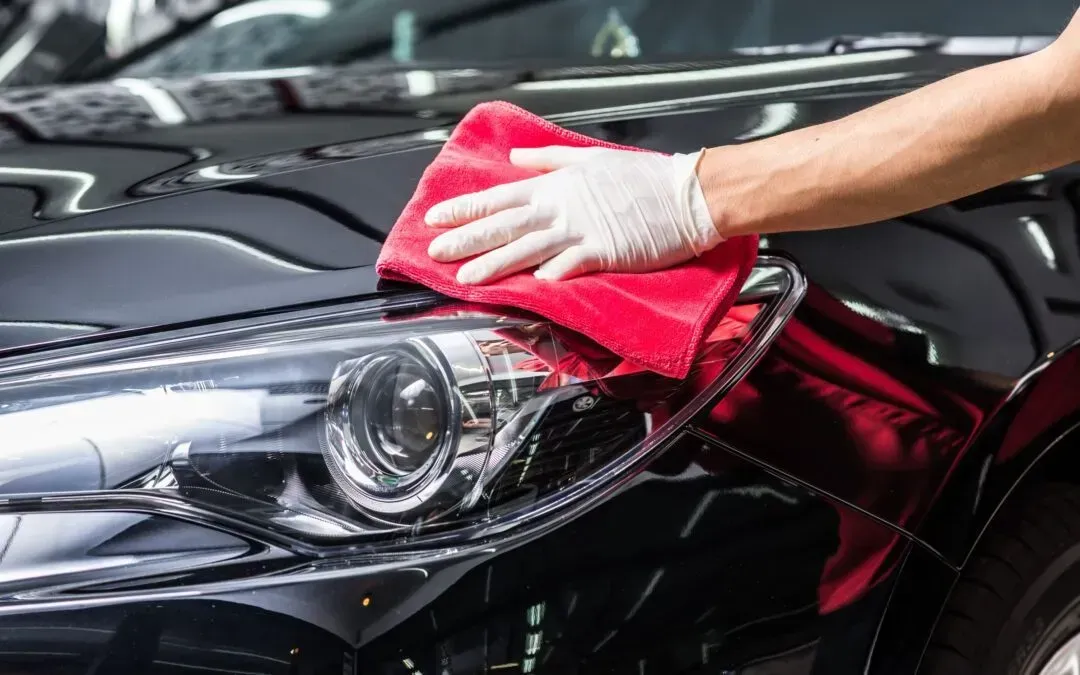 Person wearing gloves wiping a black car's headlight with a red microfiber cloth.